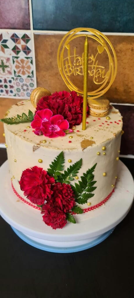 An 8 inch, 4 layers of vanilla sponge filled with homemade cherry jam and vanilla buttercream. Decorated with gold leaf, sprinkles, gold macarons, red carnations and geranium.