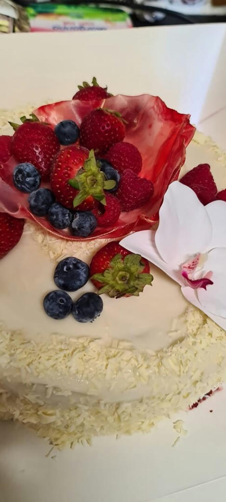 Red velvet cheesecake. Layers of moist red velvet cake with a baked vanilla cheesecake in-between, cream cheese frosting coated with flakes of white chocolate. Its decorated with a rice paper bowl, fresh fruit and a single flower