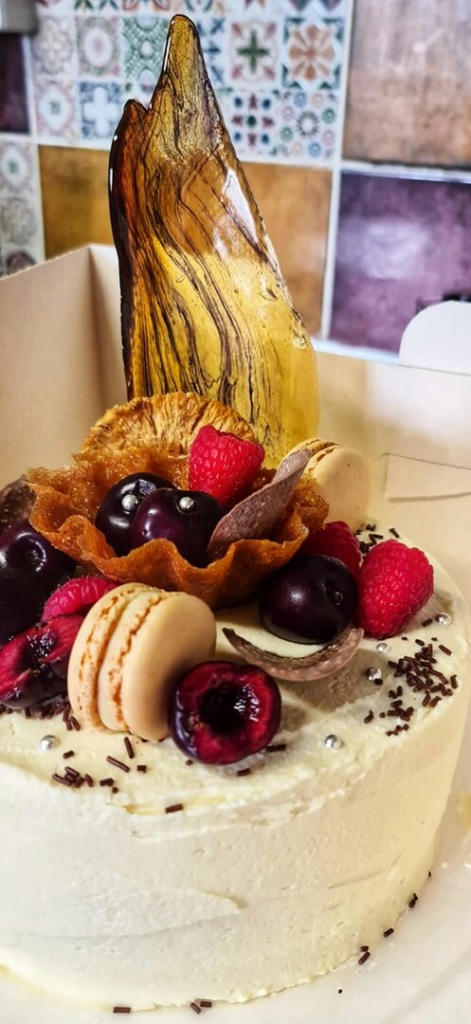 A vanilla sponge filled with vanilla buttercream and strawberry jam. The decoration has fresh cherries and raspberries, brandy snap, chocolate crisp,, macarons and a sugar shard.